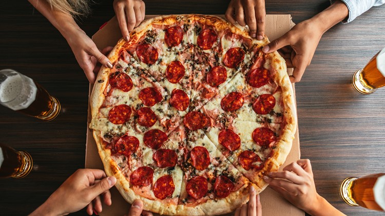 Family and friends gathered around a large pizza all grabbing a slice of delicious pepperoni pizza.
