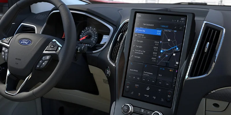 close up shot of a 2023 Ford Edge dash. You can see the iPad size touch screen infotainment system , all the features available on the steering wheel, and the speedometer.