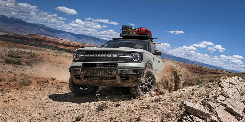 brand new 2023 bronco sport driving off road is a desert mountainous area kicking up dirt.